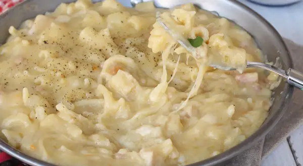 Un plat réconfortant de pasta e patate crémeux, garni de poivre noir fraîchement moulu. Une fourchette soulève une portion filante de ce délice.