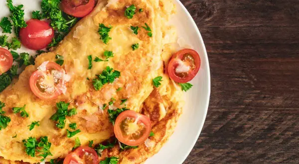 Une savoureuse omelette grecque, garnie de tomates cerises et de persil frais, sur une assiette blanche.