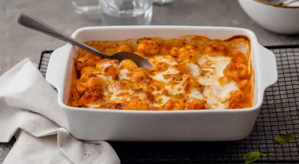 Un plat blanc rempli de gnocchi alla sorrentina, gratinés au fromage fondant et à la sauce tomate. Une cuillère est prête à servir.