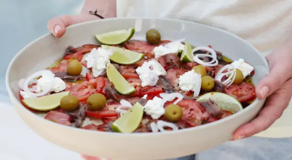 Salade colorée avec tomates, olives, anchois, oignons rouges, quartiers de citron vert et éclats de ricotta. Une idée recette ricotta fraîche et estivale.