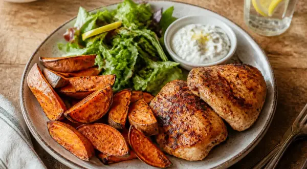 Assiette de poulet grillé avec des quartiers de patate douce rôtie, une salade verte et une sauce blanche crémeuse.