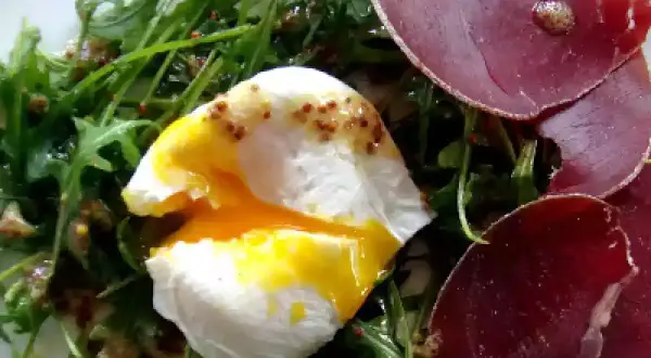 Salade lyonnaise avec œuf poché coulant, roquette et fines tranches de viande séchée.