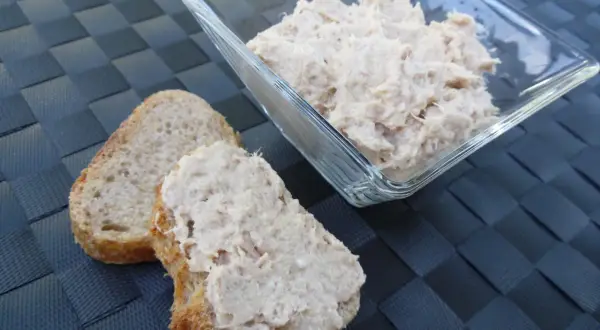 Deux tranches de pain de campagne garnies de rillettes de thon, avec un bol de rillettes de thon en arrière-plan.