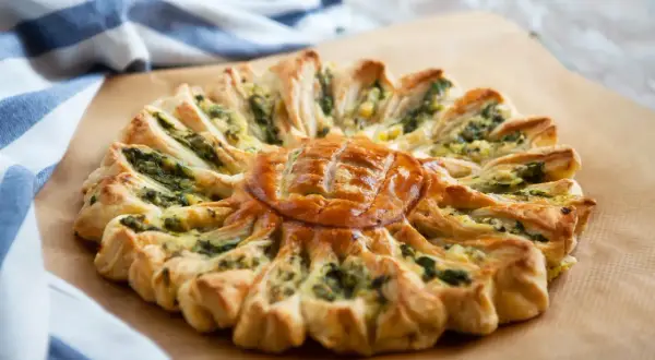Un feuilleté apéro en forme de soleil, garni d'épinards et de fromage, prêt à être dégusté.