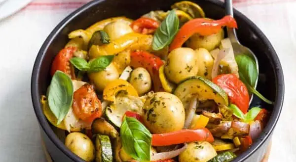 Poêlée de légumes colorés avec des pommes de terre grenaille, poivrons, courgettes et tomates, garnie de basilic frais.