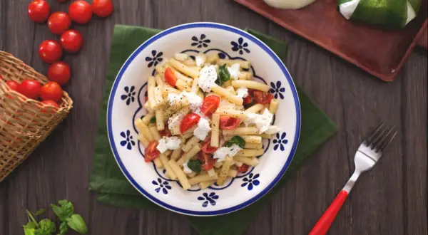 Un plat de pâtes alla checca, garni de tomates cerises fraîches, de mozzarella et de basilic, prêt à être dégusté.