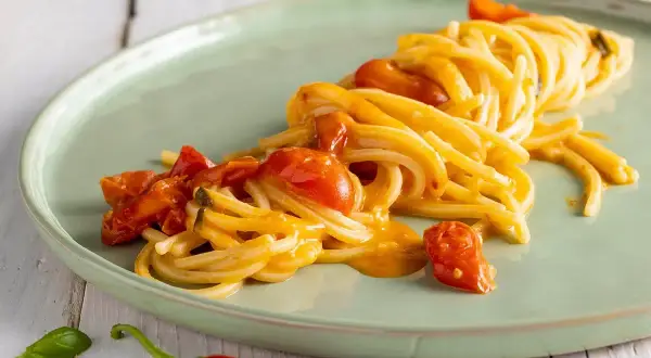 Un plat de scarpariello pasta, des spaghettis aux tomates cerises et au piment rouge, sur une assiette verte.