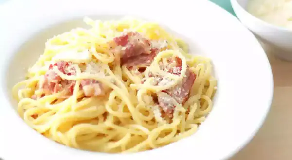 Un plat de pâtes à la carbonara crémeuses, garni de lardons croustillants et de parmesan râpé, prêt à être dégusté.