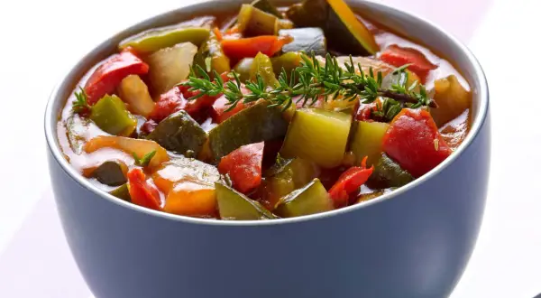 Un bol de ratatouille niçoise, un plat coloré de légumes mijotés, garni d'une branche de thym frais.