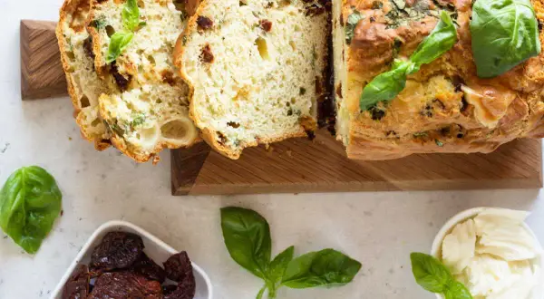 Un délicieux cake salé aux tomates séchées et basilic, parfait pour l'apéro. Des tranches sont coupées, révélant sa mie moelleuse.