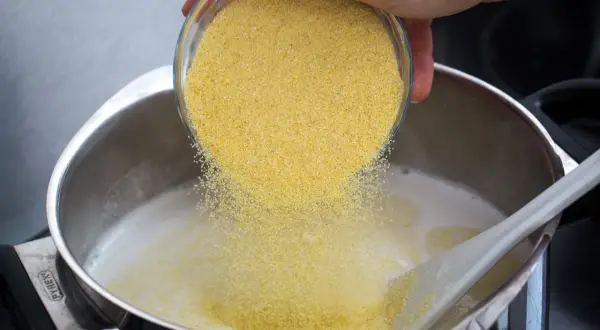 Une main verse de la semoule dans une casserole de lait chaud pour préparer un délicieux semoule au lait.
