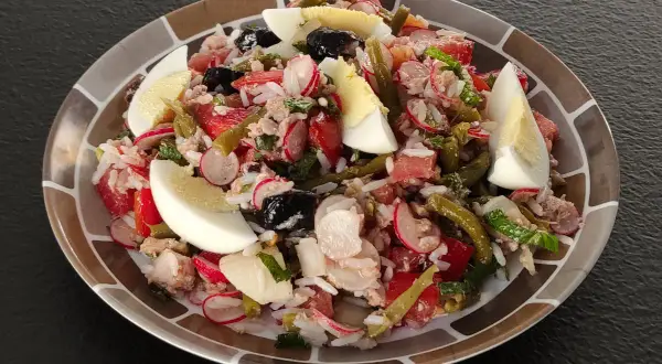Salade niçoise revisitée avec du riz, garnie d'œufs durs, de thon, de haricots verts, de tomates, de radis et d'olives noires.