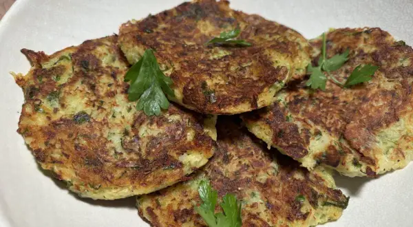 Galettes dorées de courgette et pomme de terre, garnies de persil frais, présentées dans un plat blanc.