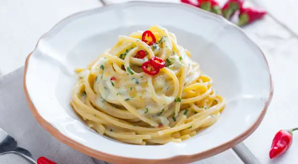 Un plat de spaghetti carrettiera crémeux, garni de piments rouges frais et de persil, prêt à être dégusté.