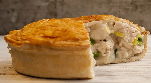 Une tourte au poulet dorée et croustillante, coupée pour révéler une garniture crémeuse et généreuse de poulet et de légumes verts.