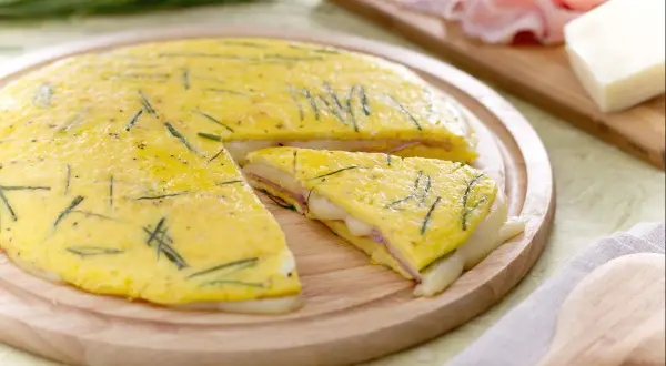 Une délicieuse omelette farcie aux herbes, jambon et fromage fondant, coupée en part pour un repas savoureux.