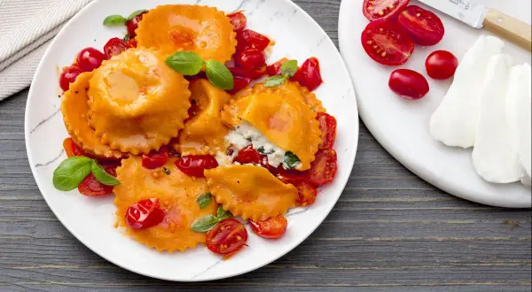 Ravioli caprese orange vif, farcis de ricotta et basilic, servis avec des tomates cerises et une sauce légère.