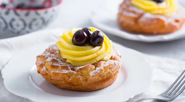 Zeppole di San Giuseppe, des pâtisseries italiennes garnies de crème pâtissière et de cerises, saupoudrées de sucre glace.