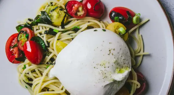 Délicieuse recette avec burrata : pâtes, tomates cerises rouges et jaunes, et herbes fraîches sur une assiette.