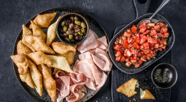 Assiette de gnocco fritto croustillant, olives, mortadelle et prosciutto, avec une salade de tomates fraîches.