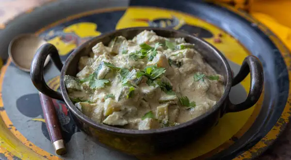 Un plat de courgettes au curry crémeux, garni de coriandre fraîche, servi dans un bol en métal sur un plateau décoré.