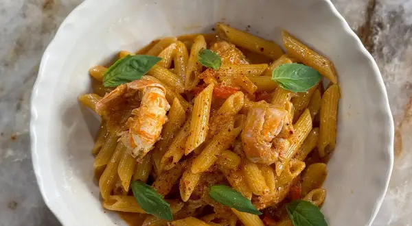 Un plat de pâtes aux langoustines, garni de feuilles de basilic frais et d'une sauce onctueuse. Un délice pour les amateurs de fruits de mer.