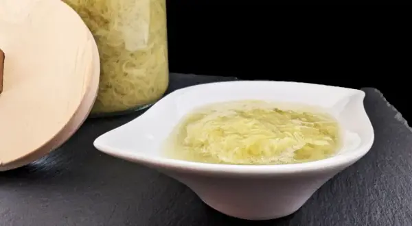 Une coupelle blanche présente une compote de rhubarbe onctueuse, avec un bocal en verre rempli de cette même compote en arrière-plan.