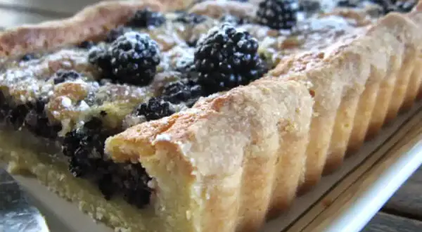 Tarte rectangulaire aux mûres, saupoudrée de sucre glace. Une délicieuse recette de tarte aux mûres, parfaite pour l'été.