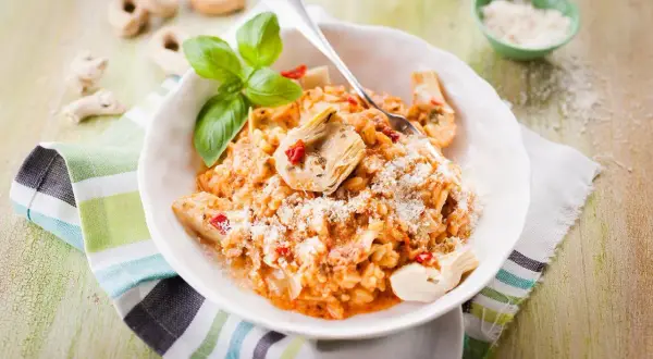Un délicieux risotto pesto rosso, garni d'artichauts et de basilic frais, saupoudré de parmesan.