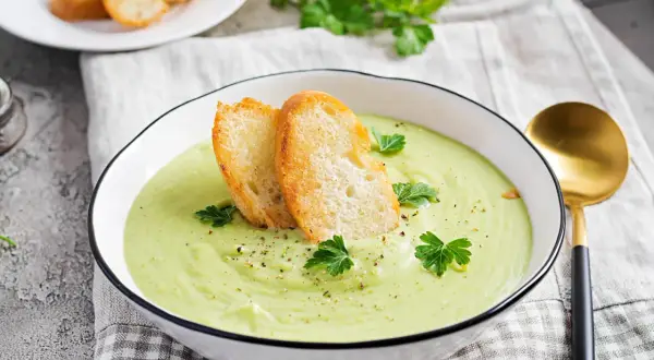 Un bol de soupe verte onctueuse, garnie de croûtons dorés et de persil frais. Parfait pour une recette gaspacho méditerranéen.