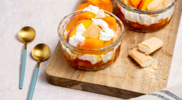 Deux coupes de dessert healthy aux pêches et crème fouettée, garnies de biscuits à la cuillère.