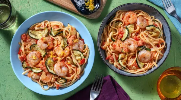 Deux assiettes de linguine crevettes courgettes, garnies de zeste de citron. Un plat savoureux et coloré.