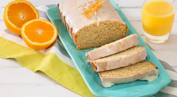 Un délicieux pain d'orange glacé, garni de zestes d'orange, servi avec des moitiés d'orange et un verre de jus d'orange.