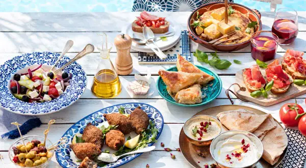 Idée apéro rapide sans cuisson : salade grecque, houmous, pain pita, feuilletés, bruschettas et olives, le tout près d'une piscine.