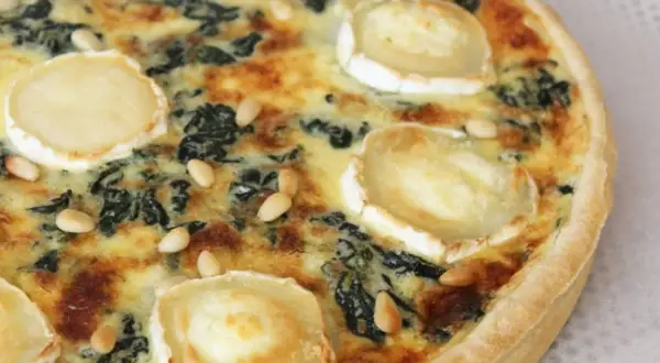 Quiche épinard chèvre, garnie de rondelles de fromage de chèvre et de pignons de pin, prête à être dégustée.