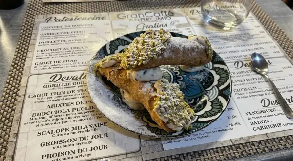 Deux cannoli siciliens garnis de crème et de pistaches concassées, saupoudrés de sucre glace.