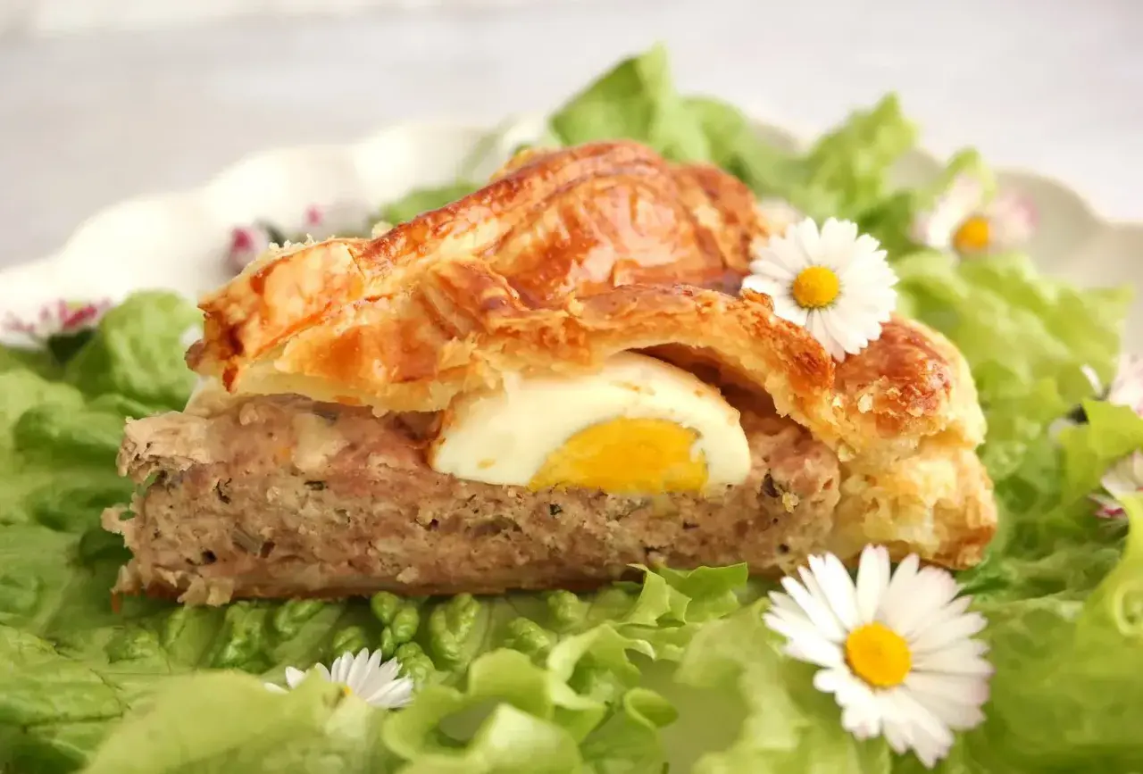 Tranche de pâté de Pâques savoureux, garni d'un œuf dur, sur un lit de salade verte et décoré de pâquerettes.