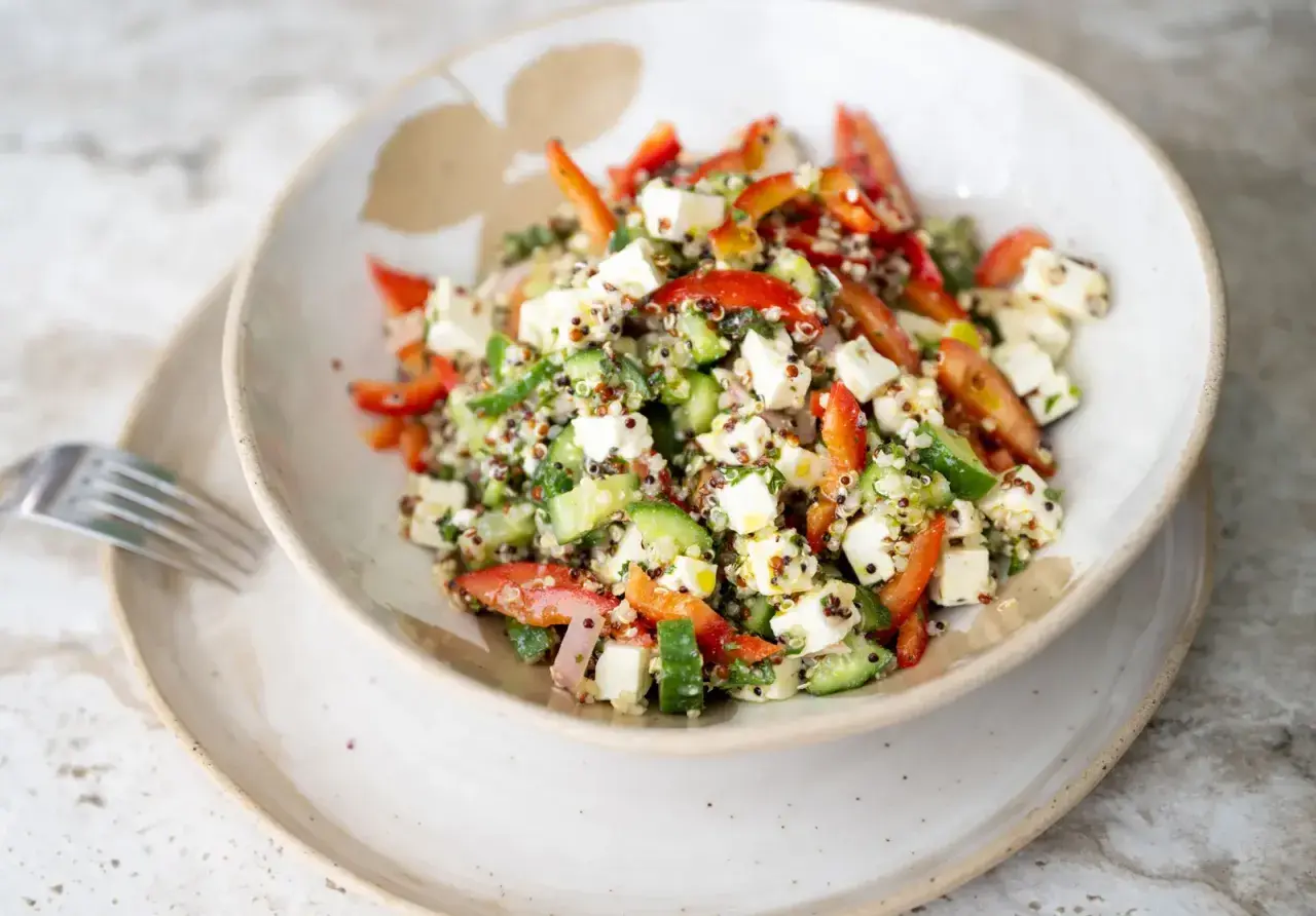 Salade quinoa colorée avec des dés de feta, concombre, poivrons rouges et herbes fraîches. Un plat sain et savoureux.