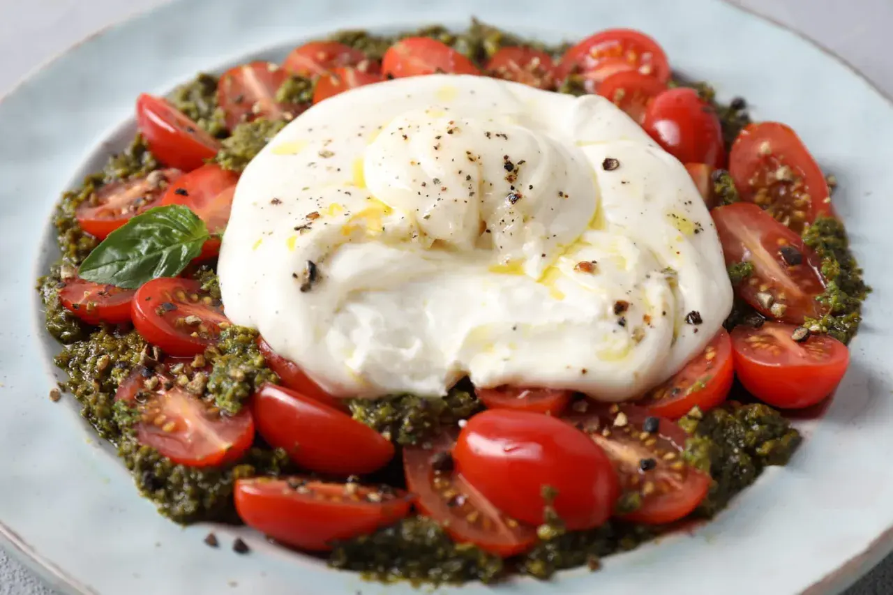 Une délicieuse recette burrata froide avec des tomates cerises coupées, du pesto et une touche de poivre noir.