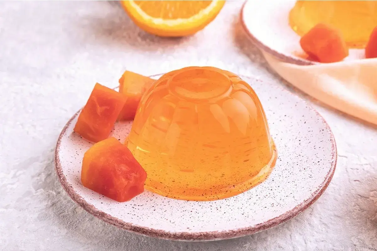 Une gelée orange brillante, servie avec des morceaux de fruits, parfaite pour apprendre comment faire de la gelée maison.
