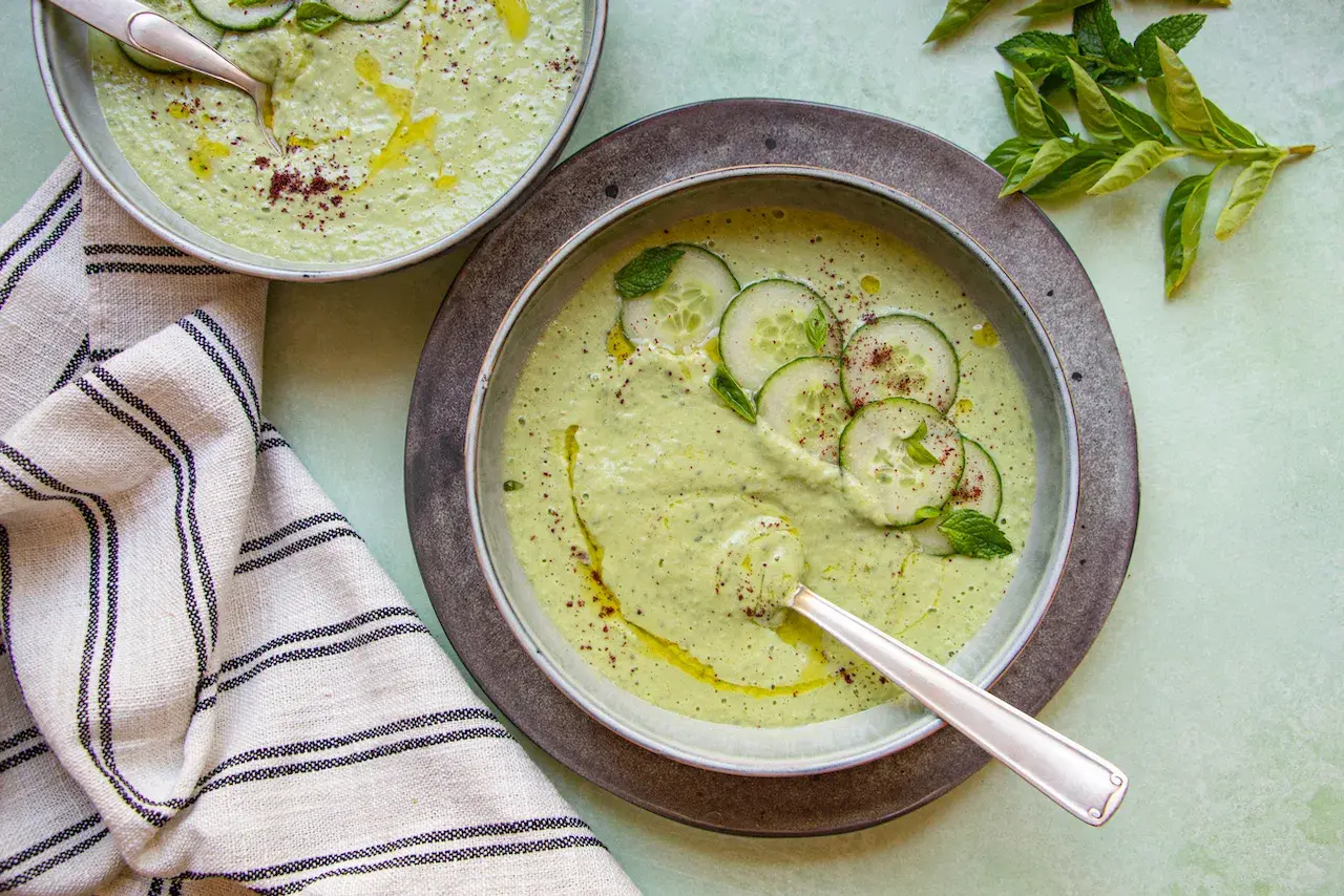 Deux bols de soupe froide crémeuse aux concombres, garnie de rondelles de concombre, de menthe et d'un filet d'huile d'olive.