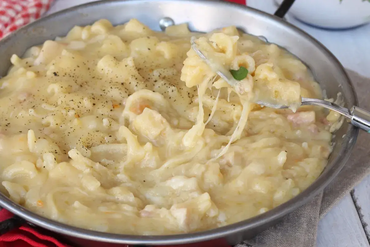 Un plat réconfortant de pasta e patate crémeux, garni de poivre noir fraîchement moulu. Une fourchette soulève une portion filante de ce délice.