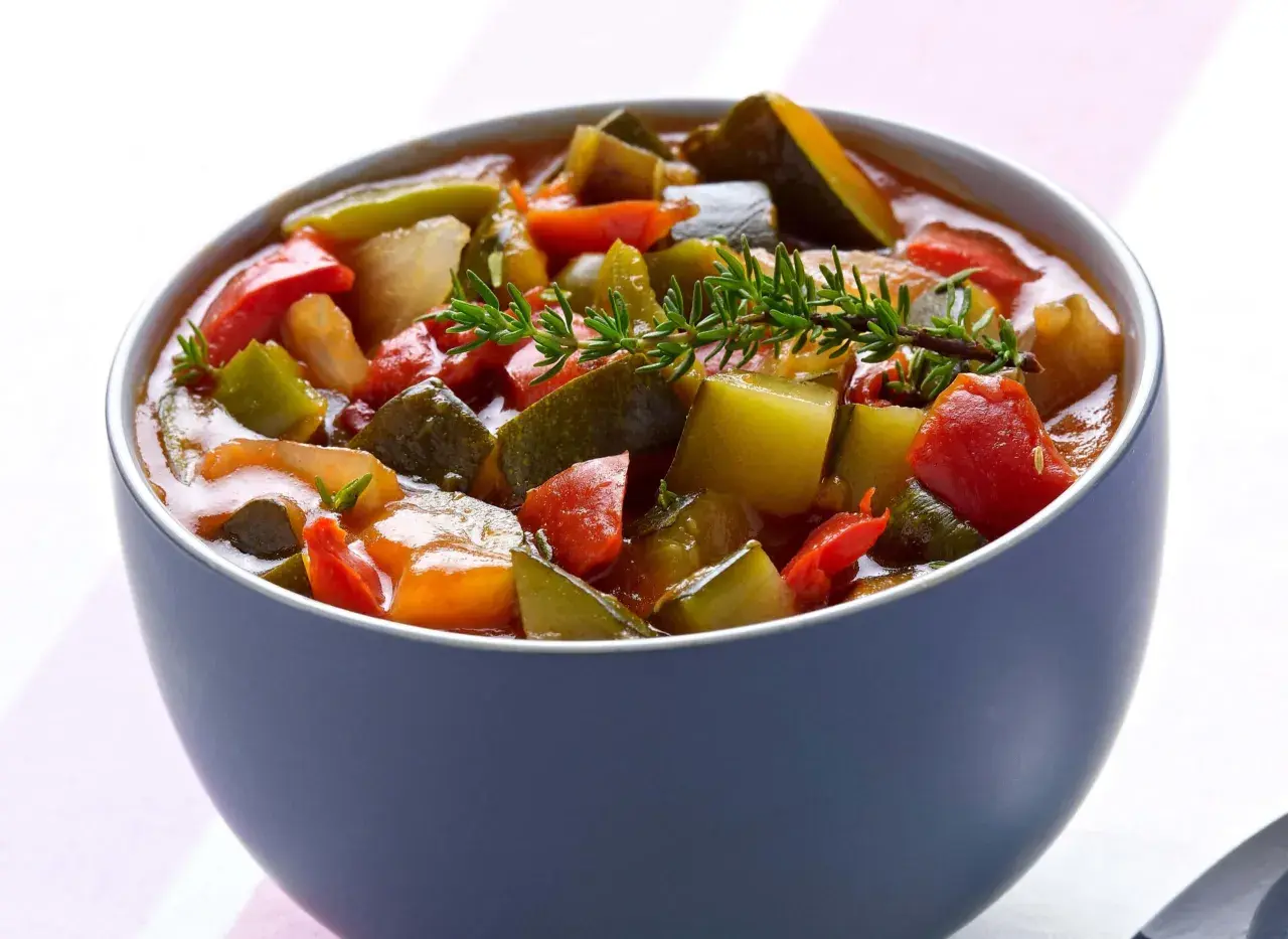Un bol de ratatouille niçoise, un plat coloré de légumes mijotés, garni d'une branche de thym frais.
