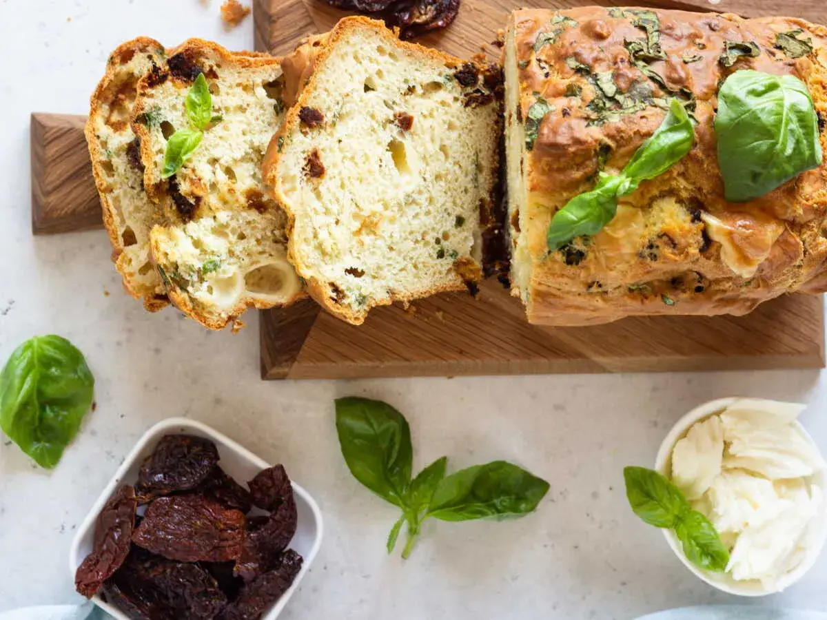 Un délicieux cake salé aux tomates séchées et basilic, parfait pour l'apéro. Des tranches sont coupées, révélant sa mie moelleuse.