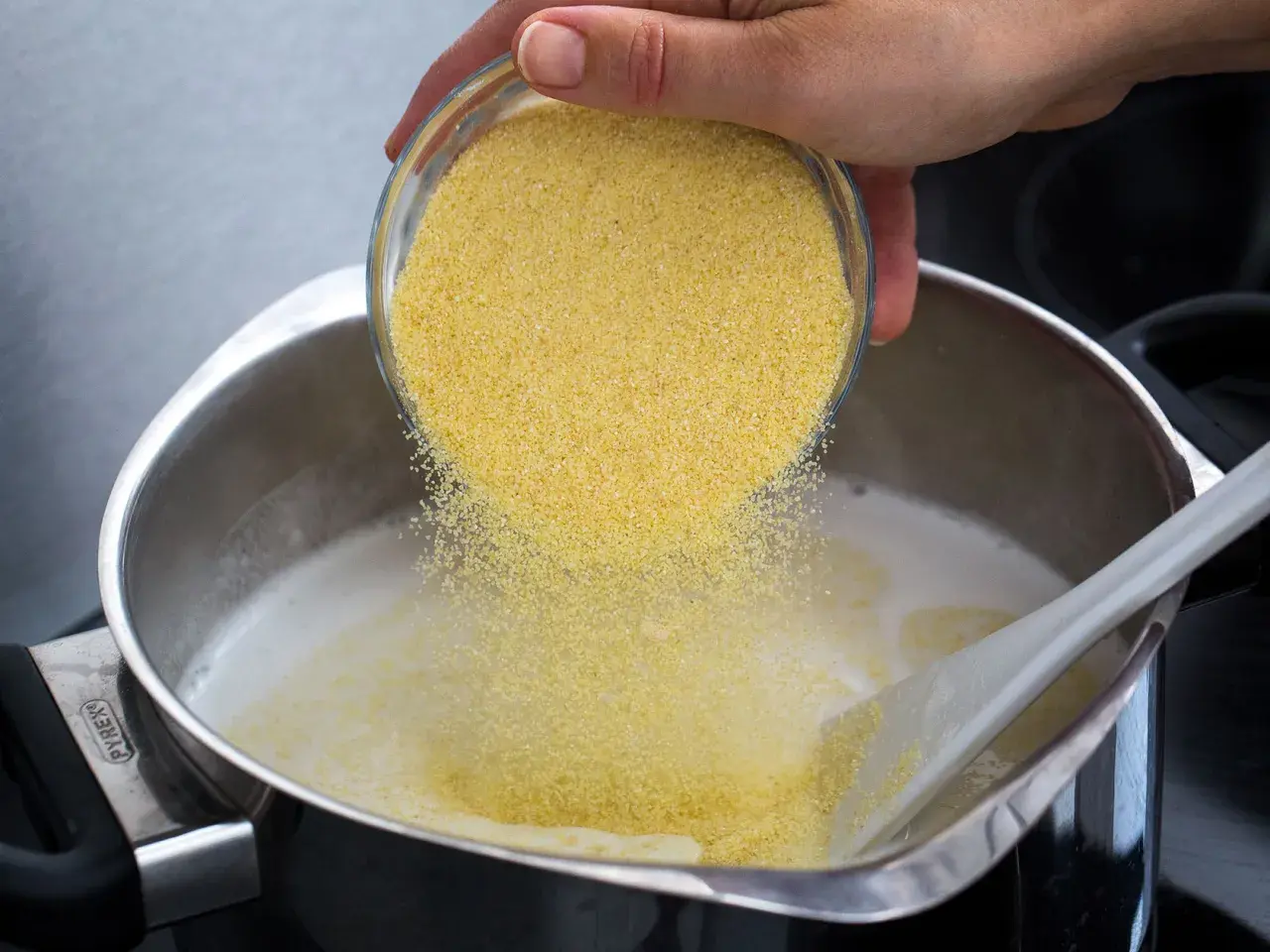 Une main verse de la semoule dans une casserole de lait chaud pour préparer un délicieux semoule au lait.