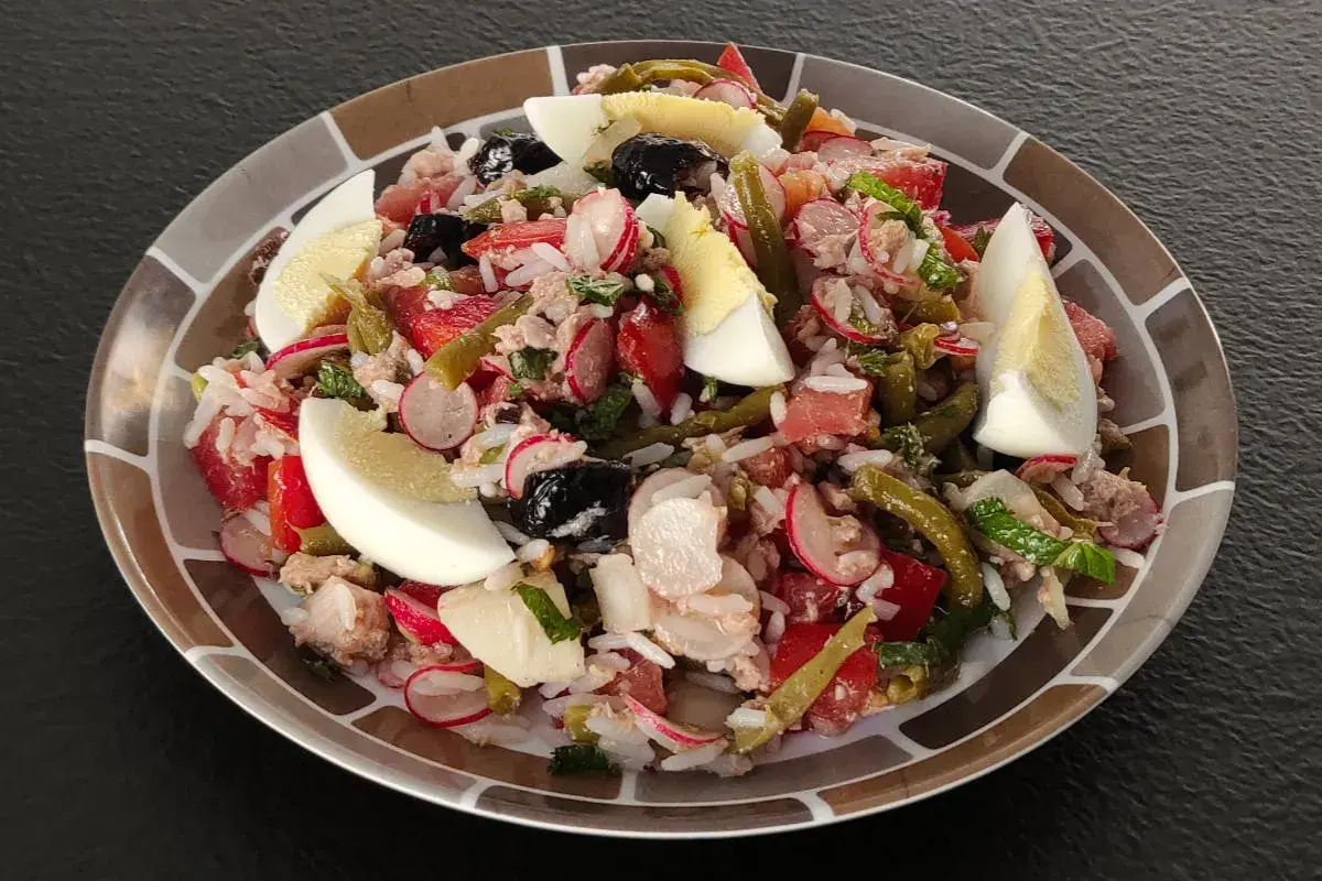 Salade niçoise revisitée avec du riz, garnie d'œufs durs, de thon, de haricots verts, de tomates, de radis et d'olives noires.