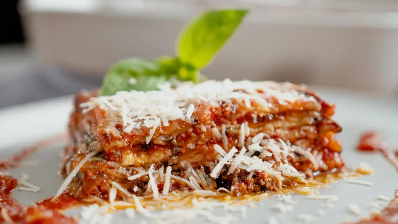 Tranche d'aubergine parmigiana, garnie de parmesan râpé et d'une feuille de basilic frais. Un délice italien.