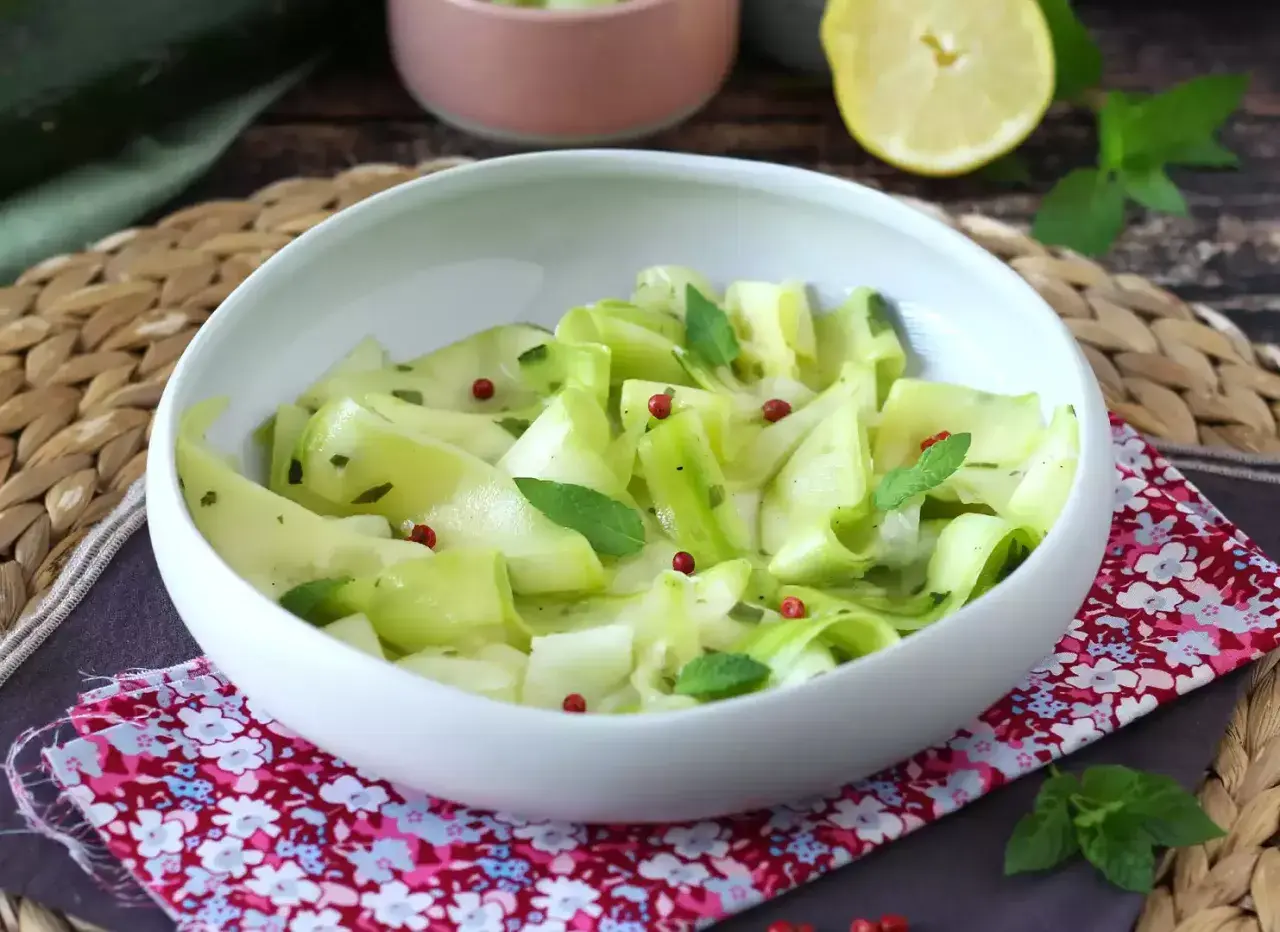 Salade fraîche de courgettes crues marinées au vinaigre, parsemée de baies roses et de menthe.