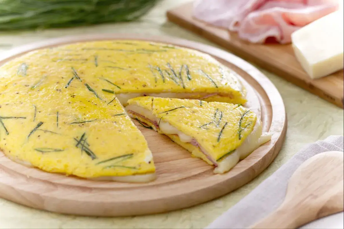 Une délicieuse omelette farcie aux herbes, jambon et fromage fondant, coupée en part pour un repas savoureux.