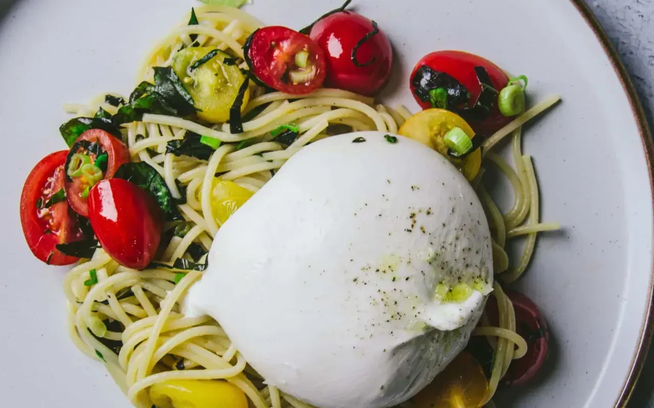 Délicieuse recette avec burrata : pâtes, tomates cerises rouges et jaunes, et herbes fraîches sur une assiette.